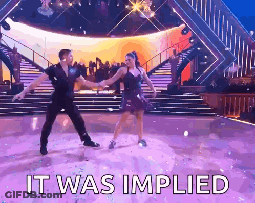 A Man And A Woman Are Dancing On A Stage With The Words It Was Implied Above Them GIF