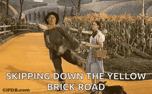 A Man And A Woman Are Dancing On A Yellow Brick Road GIF