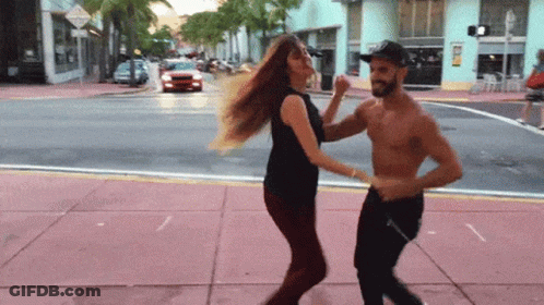 A Man And A Woman Are Dancing On The Sidewalk On A City Street GIF