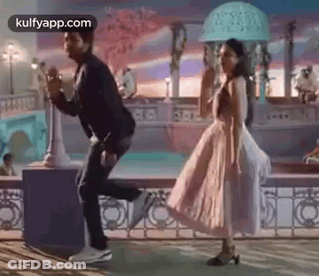 A Man And A Woman Are Dancing Together In A Park . The Woman Is Wearing A Pink Dress . GIF