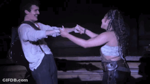 A Man And A Woman Are Dancing Together On A Stage In A Dark Room . GIF