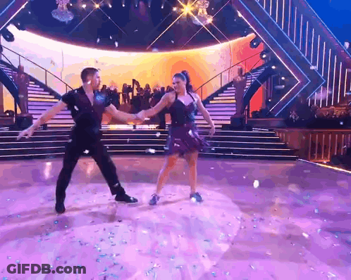 A Man And A Woman Are Dancing Together On A Stage GIF