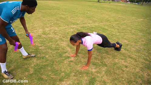A Man And A Woman Are Doing Push Ups On A Grassy Field GIF