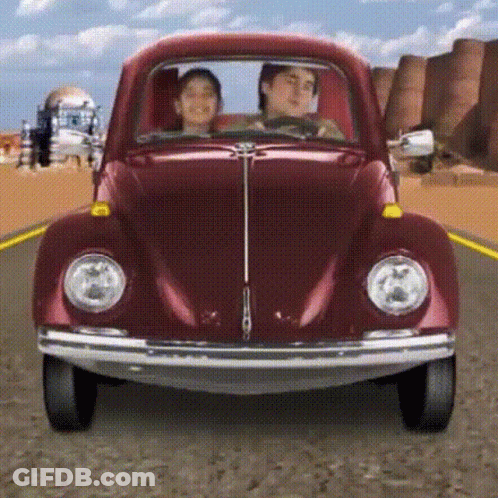 A Man And A Woman Are Driving A Red Beetle On A Road GIF
