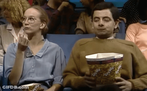 A Man And A Woman Are Eating Popcorn In A Theater . GIF