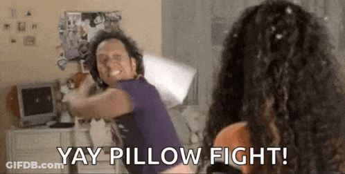 A Man And A Woman Are Having A Pillow Fight In A Room . GIF