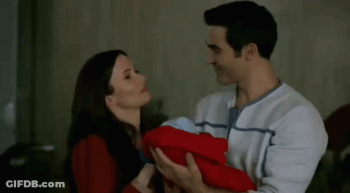 A Man And A Woman Are Holding A Baby And Kissing . GIF