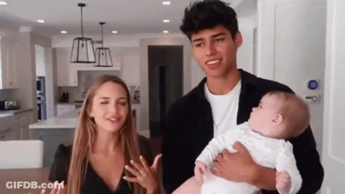 A Man And A Woman Are Holding A Baby In A Kitchen . GIF