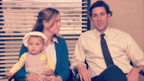A Man And A Woman Are Holding A Baby In Front Of A Window GIF