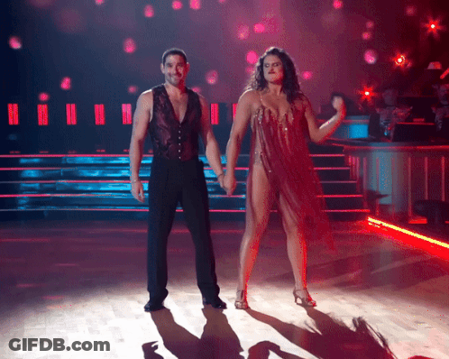 A Man And A Woman Are Holding Hands While Dancing On A Stage GIF