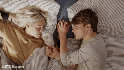 A Man And A Woman Are Holding Hands While Laying In Bed GIF