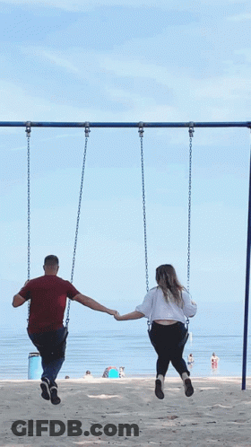 A Man And A Woman Are Holding Hands While Sitting On Swings GIF