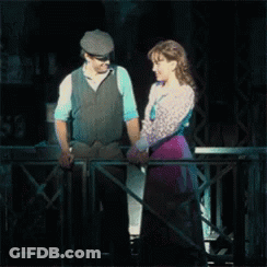 A Man And A Woman Are Holding Hands While Standing On A Balcony GIF