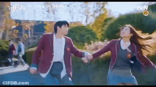 A Man And A Woman Are Holding Hands While Walking Down A Sidewalk . GIF