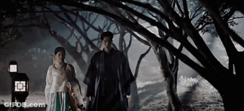 A Man And A Woman Are Holding Hands While Walking Through A Forest At Night . GIF