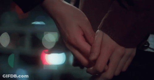 A Man And A Woman Are Holding Hands With Their Fingers Crossed . GIF