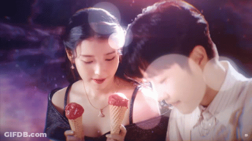 A Man And A Woman Are Holding Ice Cream Cones In Front Of Each Other . GIF
