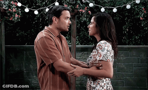 A Man And A Woman Are Hugging And Looking At Each Other In Front Of A Brick Wall GIF