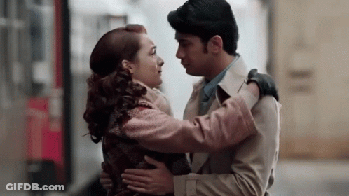A Man And A Woman Are Hugging Each Other And Kissing On A Street . GIF