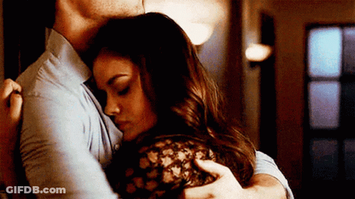 A Man And A Woman Are Hugging Each Other In A Hallway . GIF