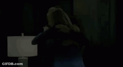 A Man And A Woman Are Hugging Each Other In A Living Room In Front Of A Lamp . GIF