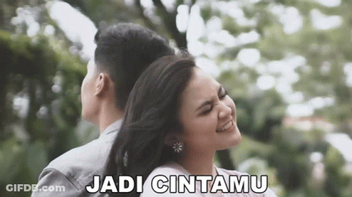 A Man And A Woman Are Hugging Each Other In A Park And The Woman Is Smiling . GIF