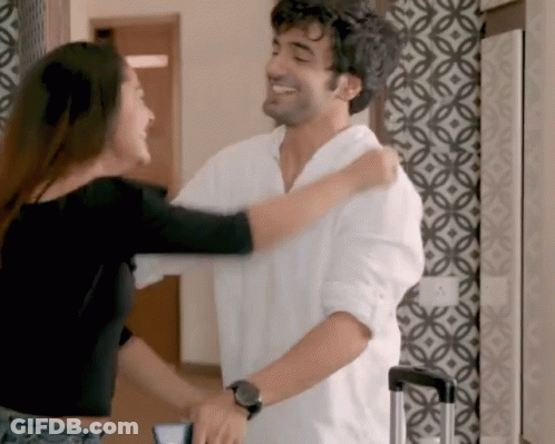 A Man And A Woman Are Hugging Each Other In A Room With A Patterned Wall . GIF