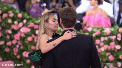 A Man And A Woman Are Hugging Each Other In Front Of Flowers GIF