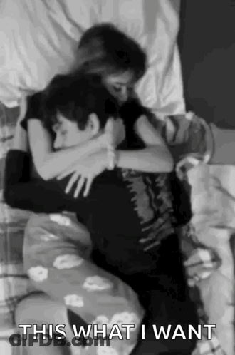 A Man And A Woman Are Hugging Each Other On A Bed In A Black And White Photo . GIF