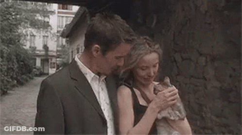 A Man And A Woman Are Hugging Each Other While Standing Next To A Stone Wall . GIF