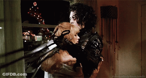 A Man And A Woman Are Hugging Each Other With A Christmas Tree In The Background Behind Them GIF