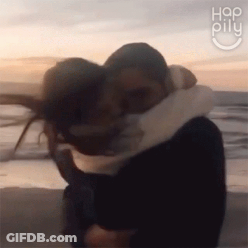 A Man And A Woman Are Hugging On A Beach . GIF