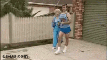 A Man And A Woman Are Jogging Down A Sidewalk . GIF