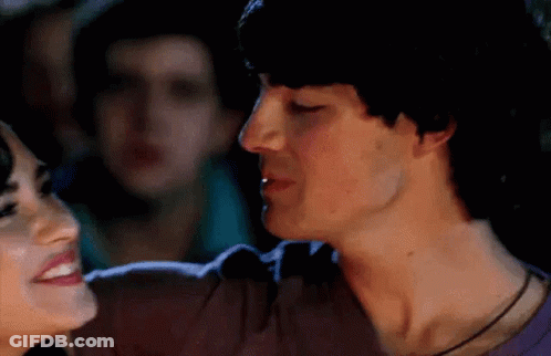 A Man And A Woman Are Kissing Each Other In A Crowded Room . GIF