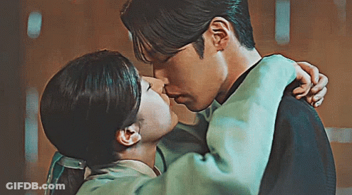 A Man And A Woman Are Kissing Each Other In A Room . GIF