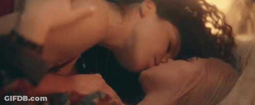 A Man And A Woman Are Kissing Each Other On A Bed . GIF