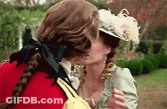 A Man And A Woman Are Kissing In A Garden . The Woman Is Wearing A Feathered Hat . GIF