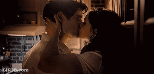 A Man And A Woman Are Kissing In A Kitchen In A Dark Room . GIF