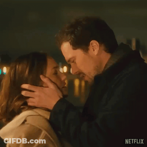 A Man And A Woman Are Kissing In Front Of A Street Light At Night . GIF