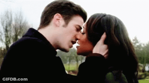 A Man And A Woman Are Kissing In Front Of Trees . GIF
