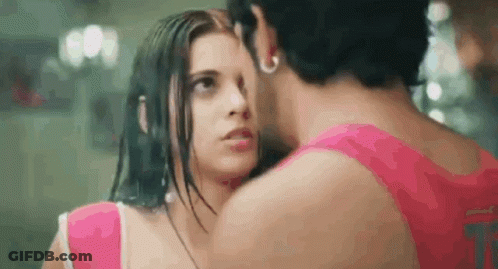 A Man And A Woman Are Kissing In The Rain And The Woman Is Wearing A Pink Top . GIF