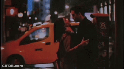 A Man And A Woman Are Kissing On A Street At Night . GIF