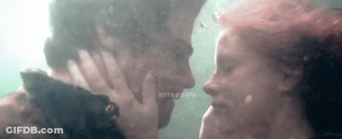 A Man And A Woman Are Kissing Underwater In The Water . GIF