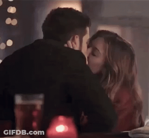 A Man And A Woman Are Kissing While Sitting At A Table In A Restaurant . GIF