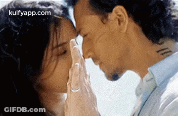 A Man And A Woman Are Kissing With Their Hands On Their Foreheads . GIF