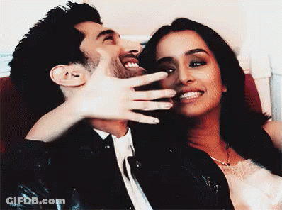 A Man And A Woman Are Laughing Together And The Woman Is Covering The Man 'S Mouth GIF