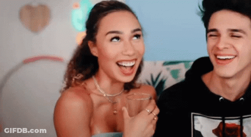 A Man And A Woman Are Laughing Together And The Woman Is Holding A Glass Of Water . GIF
