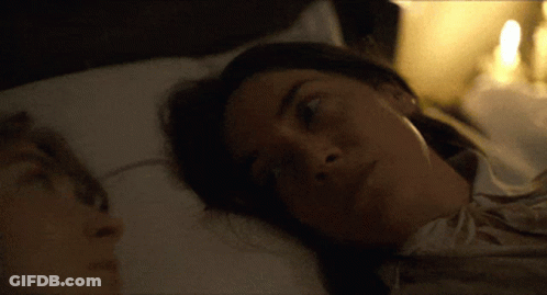 A Man And A Woman Are Laying In Bed And The Woman Is Looking At The Camera GIF