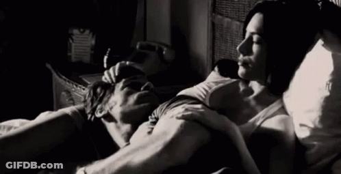 A Man And A Woman Are Laying In Bed Hugging And Kissing . GIF
