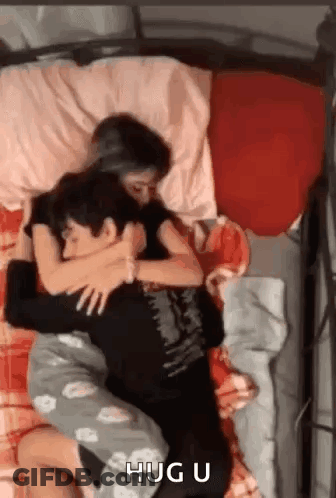 A Man And A Woman Are Laying In Bed Hugging Each Other . GIF